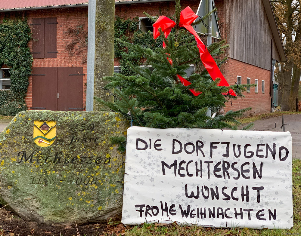 Weihnachtsgruß der Dorfjugend auf Plakat an Tannenbaum auf Verkehrsinsel